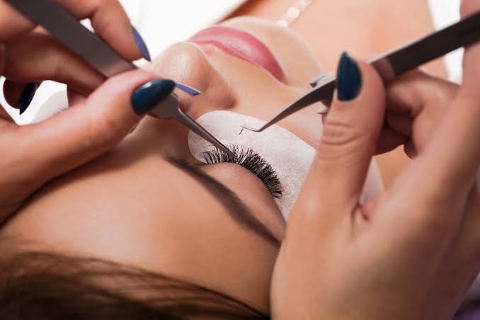 Lash artist applying extensions with precision tweezers during a fill appointment